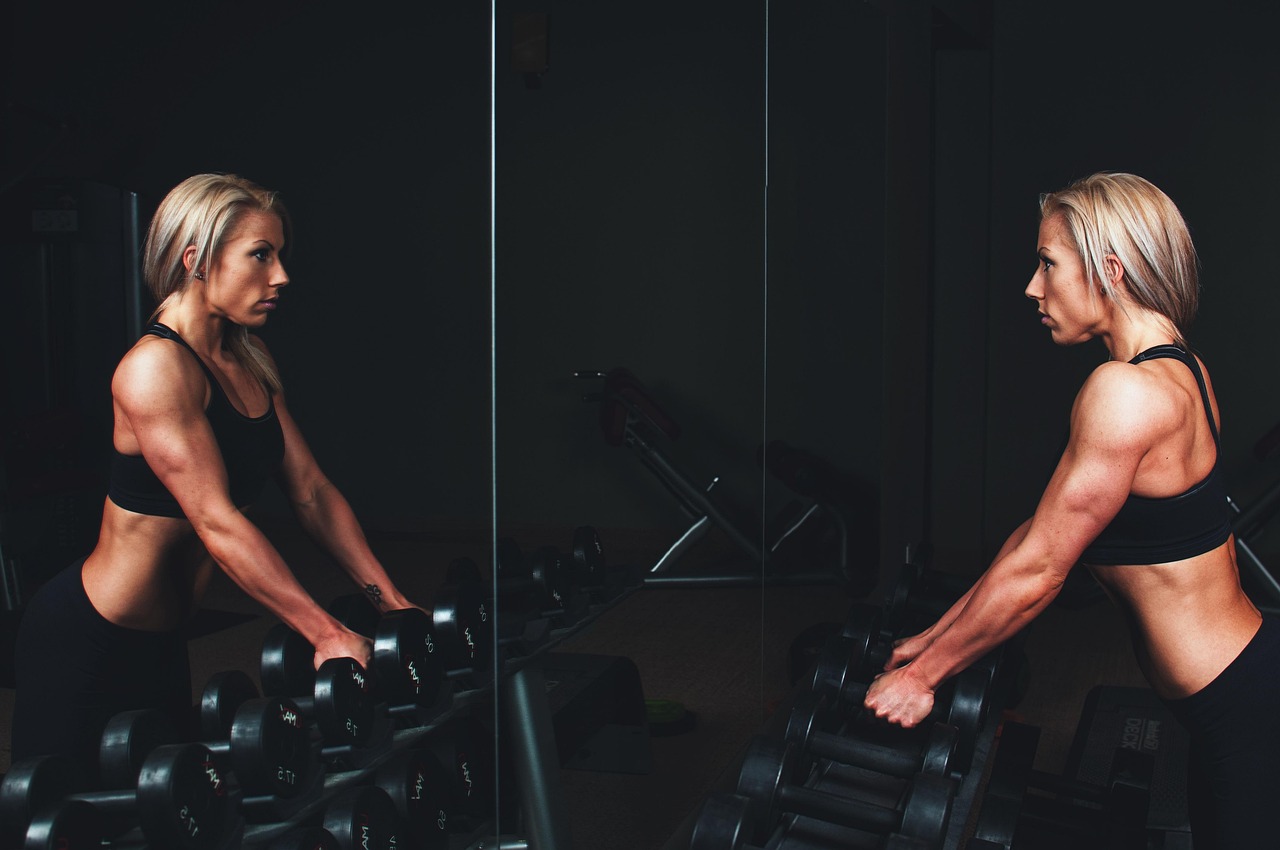 Woman lifting a dumbbell from a gym rack in front of a mirror